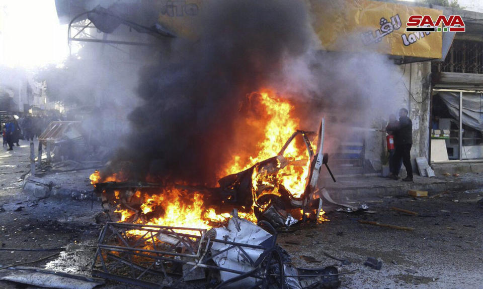 In this photo released by the Syrian official news agency SANA, a man tries to extinguishes flames rising from a burned car at the site of an explosion, in the coastal city of Latakia, Syria, Tuesday, Jan. 22, 2019. Syrian state TV said Tuesday's blast was a car bomb that went off in Al-Hammam Square in Latakia that has been a government stronghold since the conflict began in March 2011. (SANA via AP)