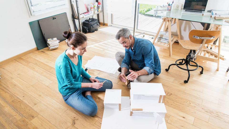 Top view. Two architects, a man and a woman working on a construction project in the office. They sit on the floor and finalize a model house.