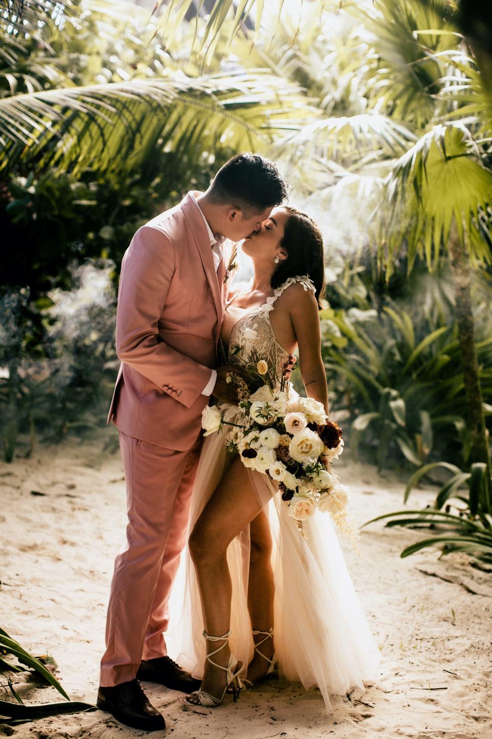 The Baks kiss in front of trees in their wedding attire