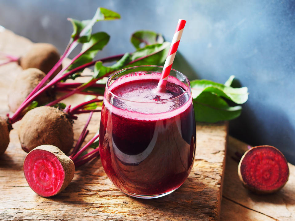 Ein Glas mit Rote-Bete-Saft auf einem Holzbrett, daneben Rote-bete-Knollen.