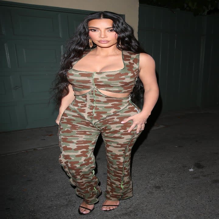 A closeup of Kim standing outside and wearing a camouflage bodysuit