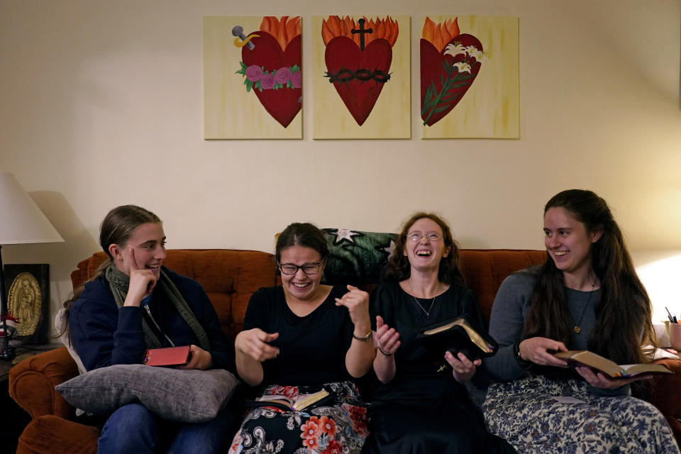 Benedictine College students from left Ashley Lestone, Hannah Moore, Niki Wood, and Madeline Hays share a laugh as they look through their prayer books before evening prayers in a room which they converted to a chapel in the house they share Sunday, Dec. 3, 2023, in Atchison, Kan. Hays takes the church’s rules seriously, from pre-marital sex to confession. She’s seriously considering becoming a nun. But she also worries about poverty and America’s wastefulness and the way Americans –including herself – can find themselves slotted into the political divide without even knowing it. (AP Photo/Charlie Riedel)