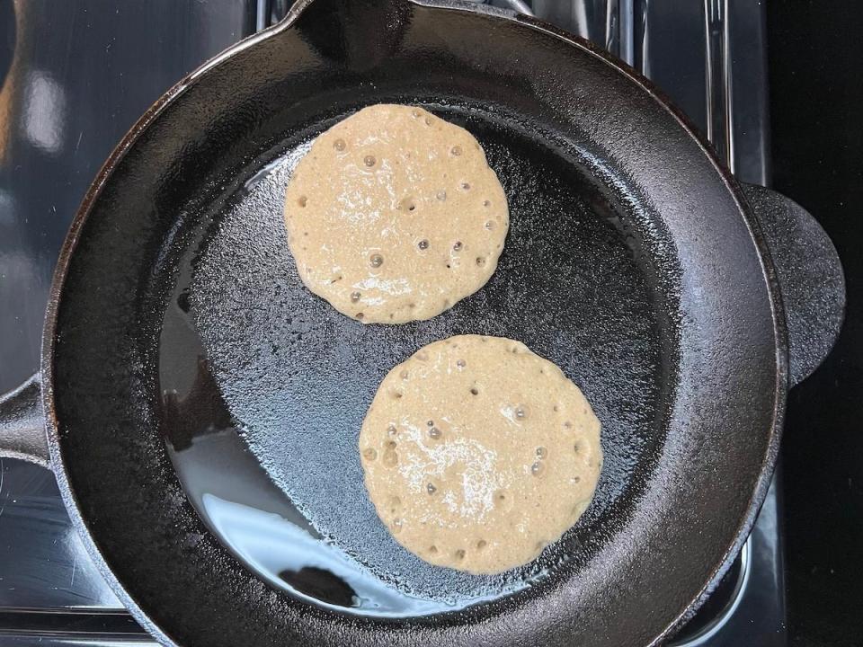 An overhead photo of two pancakes on a griddle.