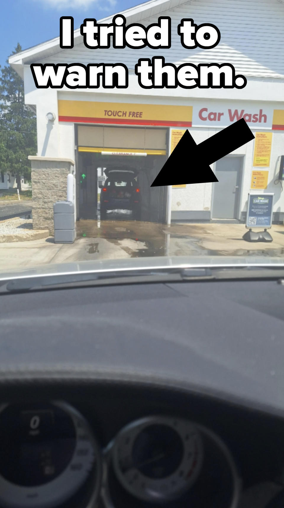 View of a car entering a touch-free car wash as seen from the inside of another car. Various instructions and signs are visible around the car wash entrance