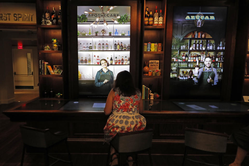 A visitor sits at a mock bar and watches interactive virtual bartenders during a media preview for the Sazerac house, in New Orleans, Tuesday, Sept. 10, 2019. Visitors to New Orleans who want to learn more about cocktails will soon have a new place to go. No, it's not another bar. The Sazerac House is a six-story building on the city's famed Canal Street owned by the Sazerac Company, a Louisiana-based spirits maker, featuring the signature New Orleans drink called the Sazerac.Tasting is encouraged, and in addition to free samples given to visitors, there will also be special classes and tastings offered daily. (AP Photo/Gerald Herbert)