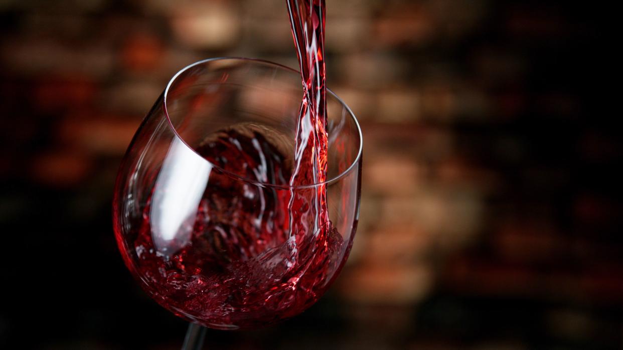 Freeze motion of red wine pouring into glass, old cellar interior.