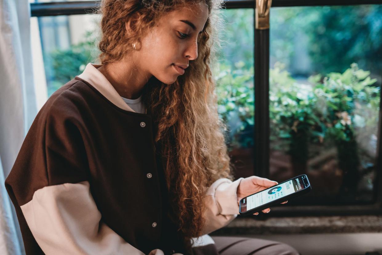 Young adult woman is checking her bank account. She's holding a smart phone with a bank mobile app.