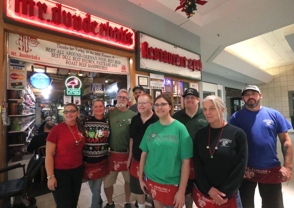 Ted Teschner, fifth from the left, owner of the Mr. Dunderbak's Bavarian Restaurant & Delicatessen at Volusia Mall in Daytona Beach, stands in front of his eatery with several of his longtime employees on Friday, Dec. 16, 2022. From left to right: Darby Neal, Katie St. Clair, Rob Pugh, Jason Burford, Teschner, Brandi Parks, Jason Budde, Dana Boothe and Kyle Shoulters.