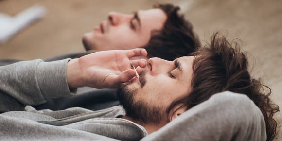 Two young men lying on the ground sharing a marijuana cigarette.