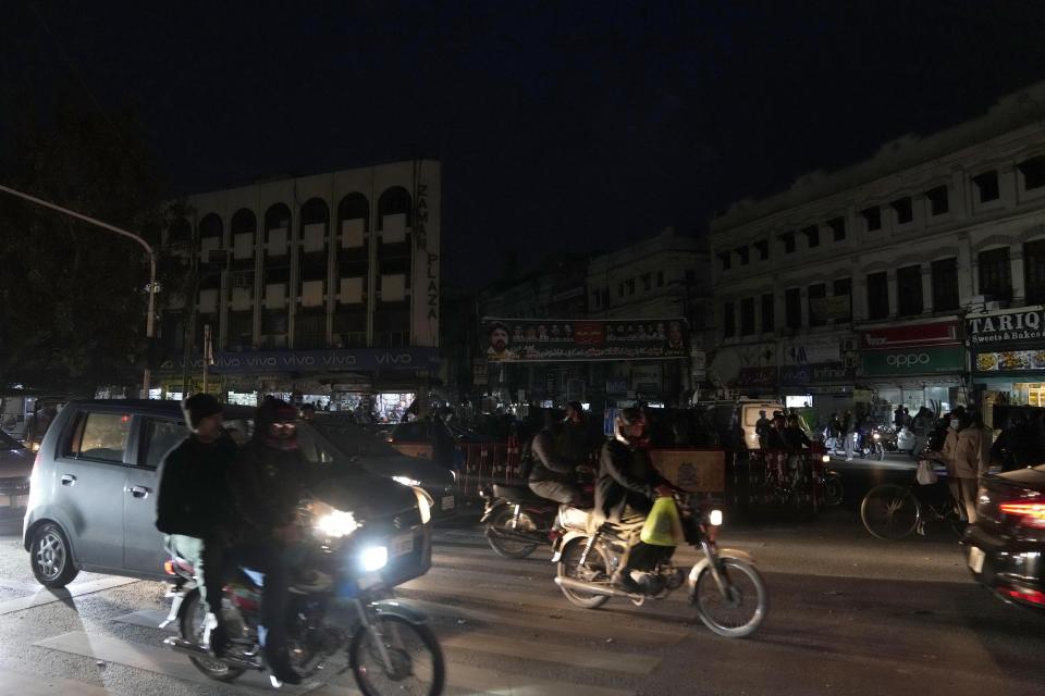 Motorcyclists and car drive on through a market where some shopkeepers use generators for electricity during a national-wide power breakdown, in Lahore, Pakistan, Monday, Jan. 23, 2023. Much of Pakistan was left without power Monday as an energy-saving measure by the government backfired. The outage spread panic and raised questions about the cash-strapped government's handling of the country's economic crisis. (AP Photo/K.M. Chaudary)