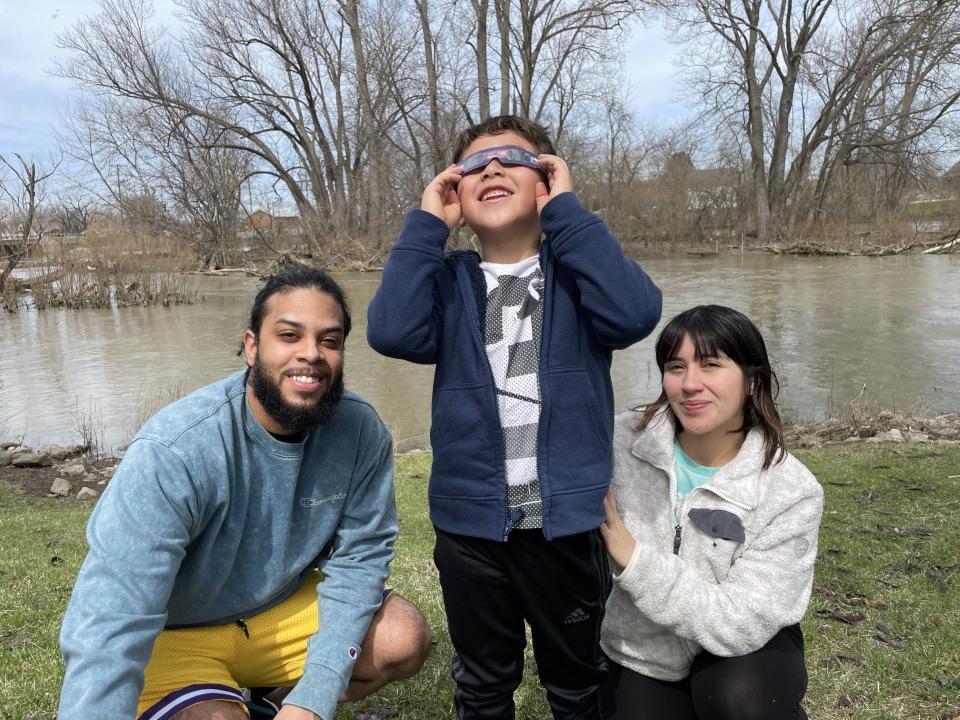 Charles Wilson (from left), Keuna Cruz and Zeyden Campell of Monroe watched the eclipse by the River Raisin Monday.