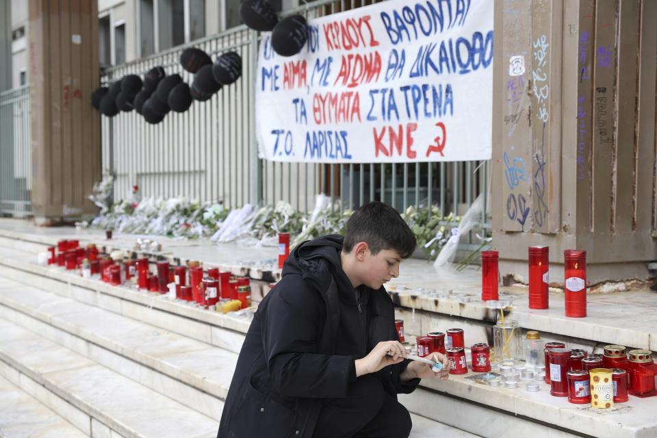 A boy lights a candle outside a court in Larissa city, about 355 kilometres (222 miles) north of Athens, Greece, Sunday, March 5, 2023. The station master involved in Greece's deadliest train crash is set to appear to a prosecutor and an examining magistrate on Sunday. (AP Photo/Vaggelis Kousioras)