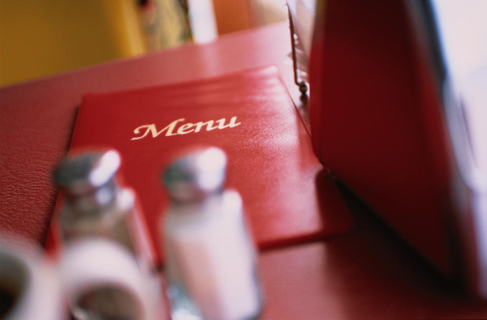 Close-up shot of a red restaurant menu on a table with salt and pepper shakers in the foreground