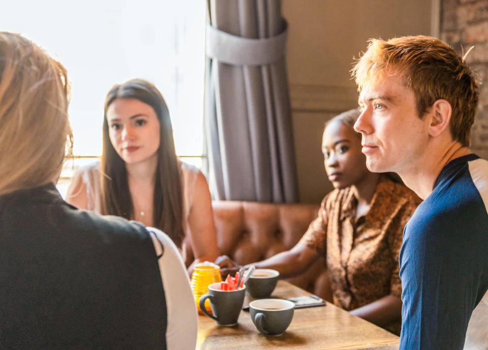 Three people listening with care to their friend as she talks in a cafe.