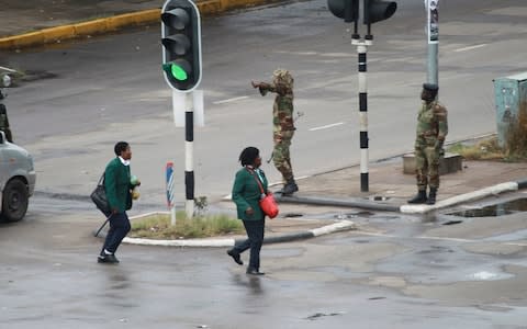 Schoolchildren seen passing military officers stationed across the capital - Credit: Tsvangirayi Mukwazhi/AP