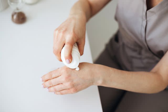 <p>Evgeniia Siiankovskaia / Getty Images</p> Female hands holding cream tube and applying it.