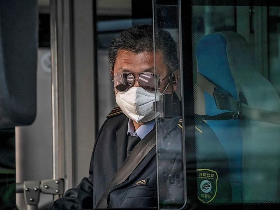 A bus driver wearing a facemask amid the concerns over the Covid-19 coronavirus drives a bus during rush hour on a street in Beijing on 7 April, 2020 (Getty Images)