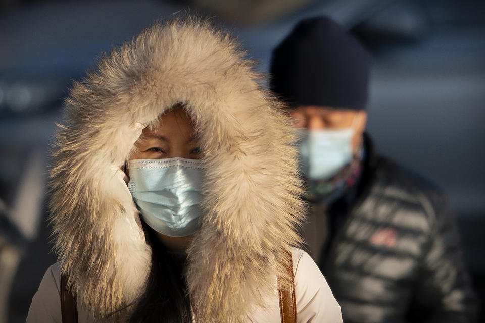 A woman wearing a face mask to protect against the spread of the coronavirus walks along a street during the morning rush hour in Beijing, Wednesday, Dec. 30, 2020. Beijing has urged residents not to leave the city during the Lunar New Year holiday in February, implementing new restrictions and mass testings after several coronavirus infections last week. (AP Photo/Mark Schiefelbein)