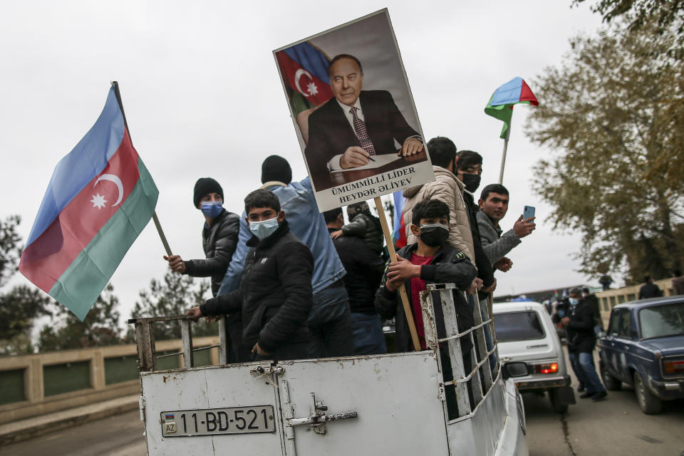 Azerbaijanis with national flags and a portraits of Azerbaijani President Ilham Aliyev's father and former Azerbaijani President Heydar Aliyev celebrate the transfer of the Lachin region to Azerbaijan's control, as part of a peace deal that required Armenian forces to cede the Azerbaijani territories they held outside Nagorno-Karabakh, in Aghjabadi, Azerbaijan, Tuesday, Dec. 1, 2020. Azerbaijan has completed the return of territory ceded by Armenia under a Russia-brokered peace deal that ended six weeks of fierce fighting over Nagorno-Karabakh. Azerbaijani President Ilham Aliyev hailed the restoration of control over the Lachin region and other territories as a historic achievement. (AP Photo/Emrah Gurel)