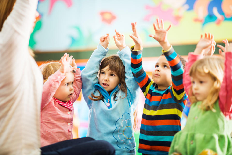 Cute children playing in the playroom with their arms raised.