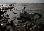 A man prays on top of his brother's grave which is inundated by sea water in Tambak Lorok village of Semarang, Indonesia, February 1, 2018. REUTERS/Beawiharta