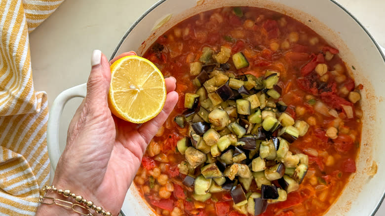 hand adding lemon to tomato eggplant stew