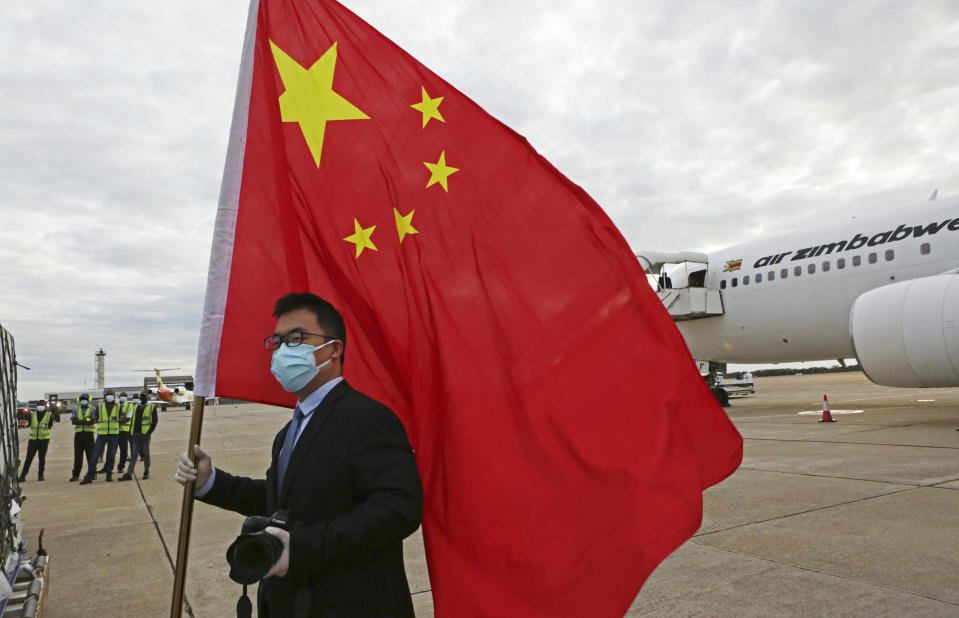 FILE - In this Monday, Feb, 15, 2021 file photo, an official from the Chinese embassy in Zimbabwe holds a Chinese flag next to a plane carrying Sinopharm COVID-19 vaccine from China upon arrival at Robert Mugabe International Airport in Harare. Zimbabwe received its first COVID-19 vaccines with the jet carrying 200,000 Sinopharm doses from China. (AP Photo/Tsvangirayi Mukwazhi)