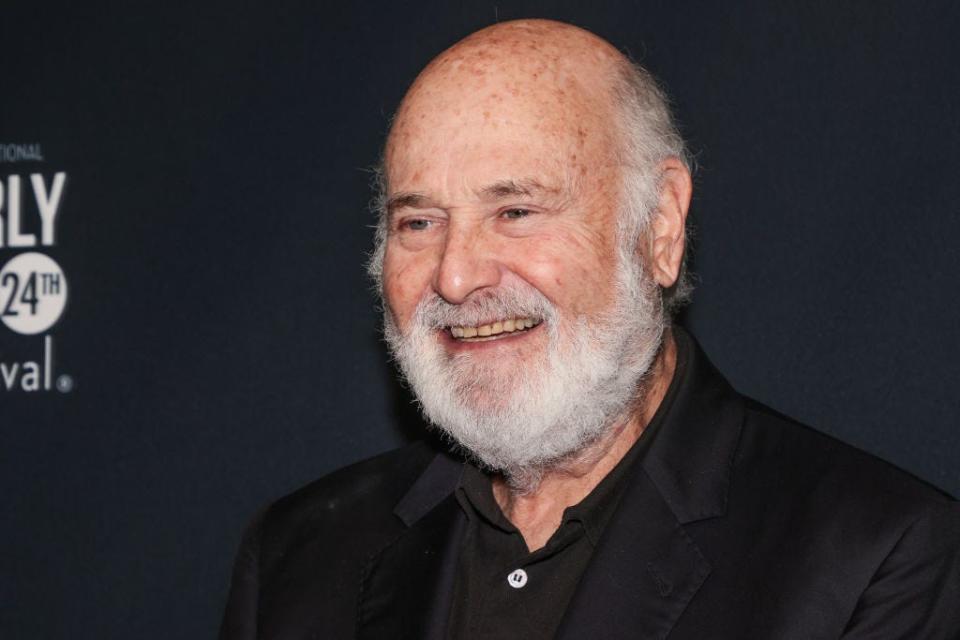 Rob Reiner smiles for cameras at an event.