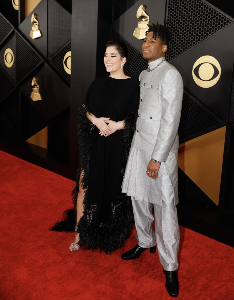 Suleika Jaouad wears a black dress and Jon Batiste wears a silver kilt