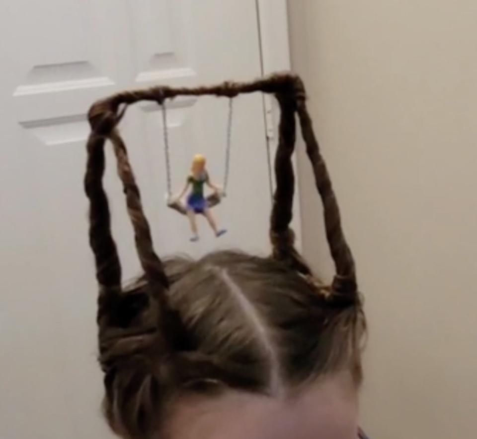 A little girl's pigtails forming the frames of a swing from which a doll sits