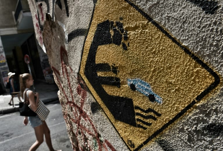 A woman walks past a wall bearing graffiti concerning Greece's possible exit from the euro in Athens on June 28, 2015