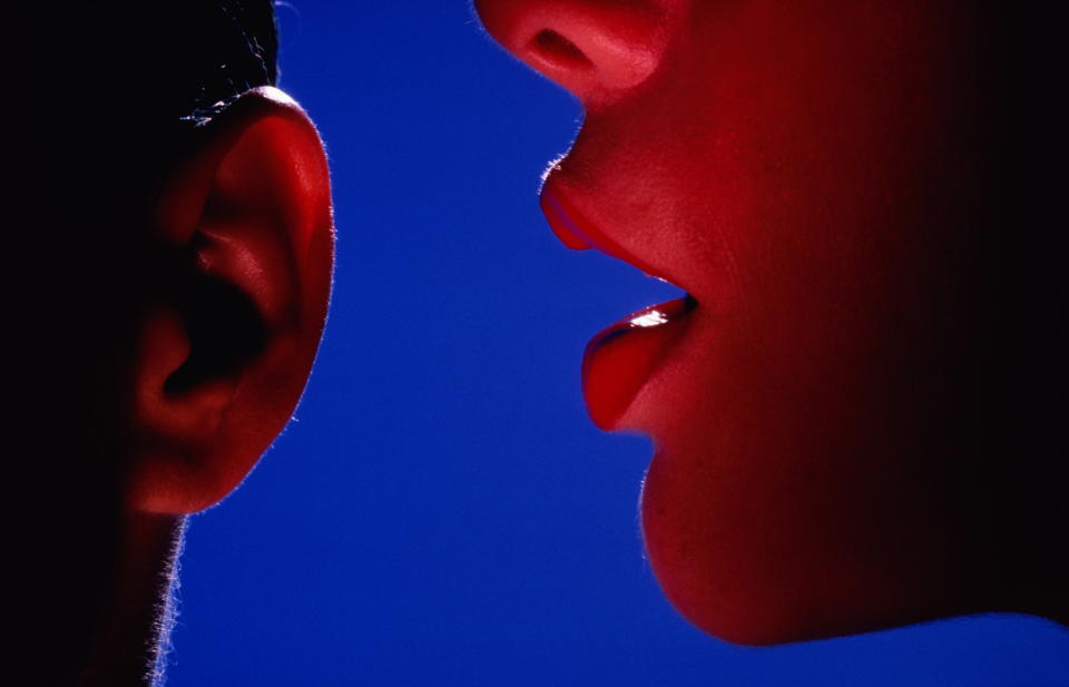 Woman whispering into man's ear, close up