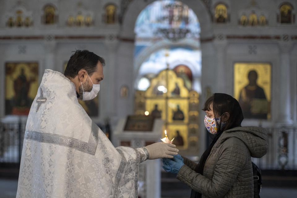 In this photo taken on Tuesday, June 2, 2020, Father Vasily Gelevan gives a candle to a daughter of a person who died of apoplexy during a funeral service at the Church of the Annunciation of the Holy Virgin in Sokolniki, in Moscow, Russia.In addition to his regular duties as a Russian Orthodox priest, Father Vasily visits people infected with COVID-19 at their homes and hospitals. (AP Photo/Alexander Zemlianichenko)