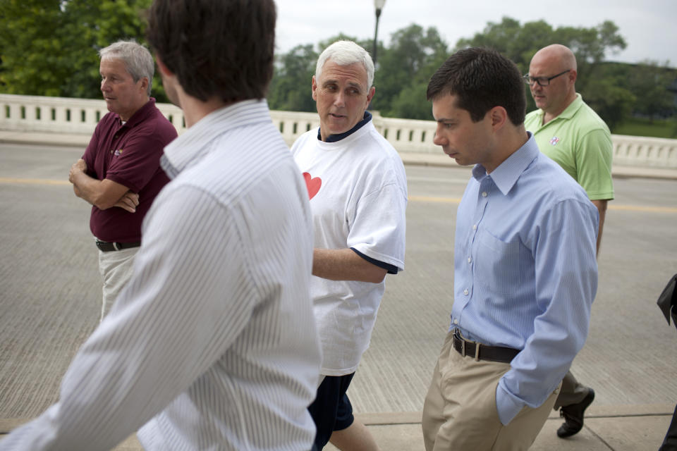 FILE - IN this July 3, 2013, file photo, then-Indiana Gov. Mike Pence, center, talks with South Bend mayor Pete Buttigieg, right, as they cross the Jefferson Boulevard bridge during a fitness walk along the St. Joseph River in downtown South Bend, Ind. Democratic presidential candidate Pete Buttigieg blasts Vice President Mike Pence’s religious conservatism. But as the mayor of South Bend, Indiana, his tone toward the state’s former governor was more muted. The two once had a cordial relationship. (James Brosher/South Bend Tribune via AP)