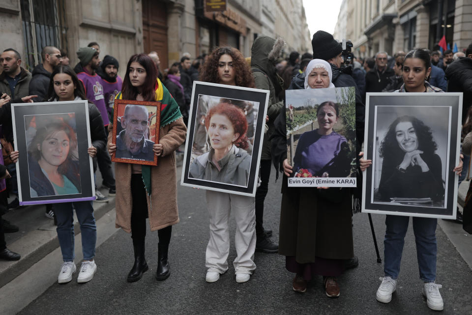 Kurdish activists holds portraits at the site where three women Kurdish activists were found shot dead in 2013, in Paris, Monday, Dec. 26, 2022 in Paris. A 69-year-old Frenchman is facing preliminary charges of racially motivated murder, attempted murder and weapons violations over Friday's shooting, prosecutors said. (AP Photo/Lewis Joly)