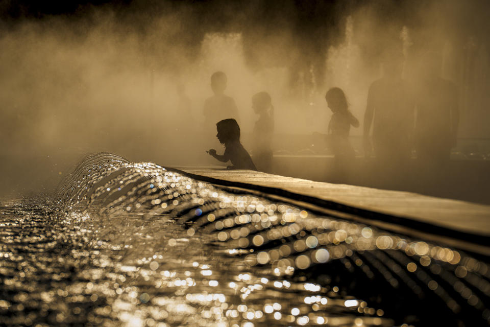 Children enjoy the drizzle from a public fountain before sunset in Bucharest, Romania, Thursday, June 20, 2024 as temperatures exceeded 38 degrees Celsius (100.4 Fahrenheit). The national weather forecaster issued a orange warning for western and southern Romania where temperatures are expected to reach 38 degrees Celsius (100.4 Fahrenheit) in the coming days. (AP Photo/Vadim Ghirda)