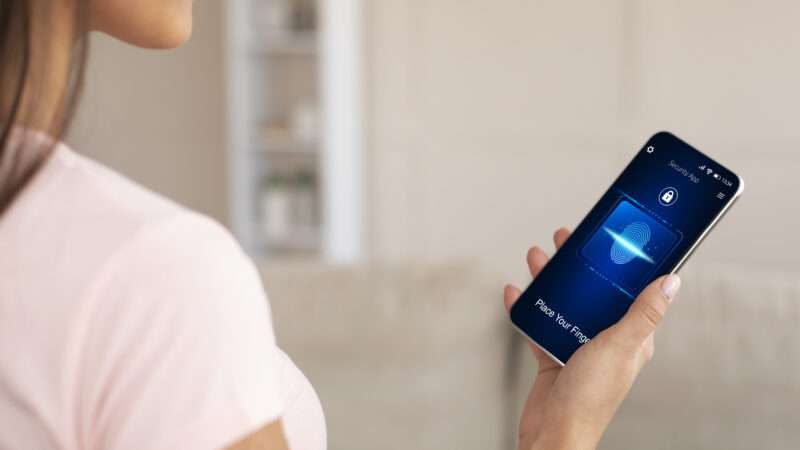 Woman holds a smartphone open to a screen that asks for her fingerprint authentication.