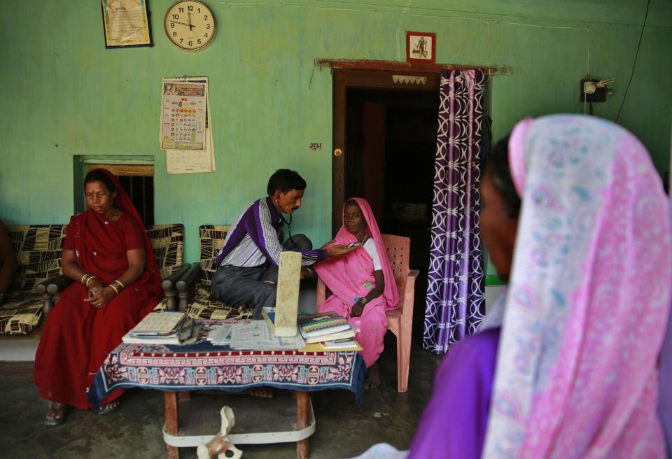 In this April 15, 2014 photo, Dr. Harihar Patel examines a woman who is suffering of breathing problem at his house Gare village near the industrial city of Raigarh, Chhattisgarh state, India. Patel, the area’s only trained doctor for 10 kilometers (six miles), said he's seen an enormous leap in the number of people with asthma and other lung ailments, skin lesions and exhaustion. (AP Photo/Rafiq Maqbool)