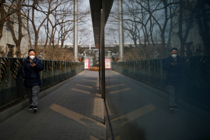 Una mujer mira su teléfono celular mientras camina junto a una parada de autobús en Pekín, China, el 27 de enero de 2020