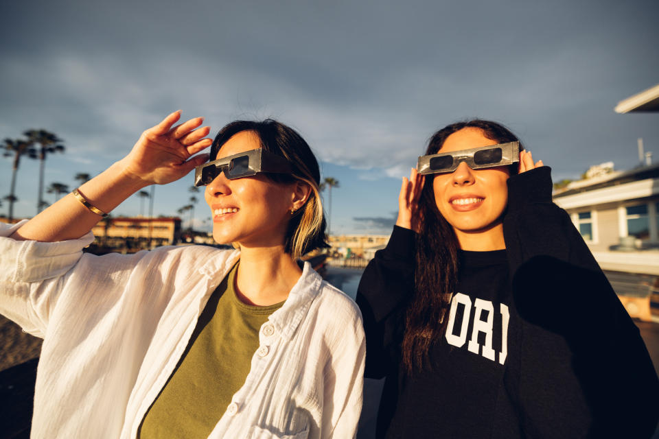 Two individuals wearing eclipse glasses looking upwards, likely viewing an eclipse