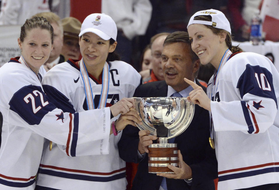 FILE - In this April 9, 2013, file photo, United States' Kacey Bellamy, Julie Chu and Meghan Duggan, from left, stand with IIHF president Rene Fasel as they are presented with the trophy after the U.S. team defeated Canada 3-2 in the gold medal game at the women's ice hockey world championships in Ottawa, Ontario. The women’s world hockey championships in Canada have been canceled because of the new coronavirus. International Ice Hockey Federation President René Fasel tells The Associated Press the decision was made by conference call Saturday, March 7, 2020. (Sean Kilpatrick/The Canadian Press via AP, File)