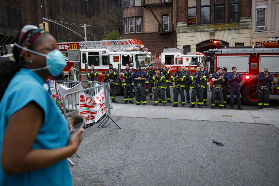 FILE - In this April 14, 2020, file photo FDNY firefighters gather to applaud medical workers as attending physician Mollie Williams, left, wears personal protective equipment due to COVID-19 concerns outside Brooklyn Hospital Center in New York. Essential workers are lauded for their service and hailed as everyday heroes. But in most states nurses, first responders and frontline workers who get COVID-19 on the job have no guarantee they'll qualify for workers' comp to cover lost wages and medical care. (AP Photo/John Minchillo, File)