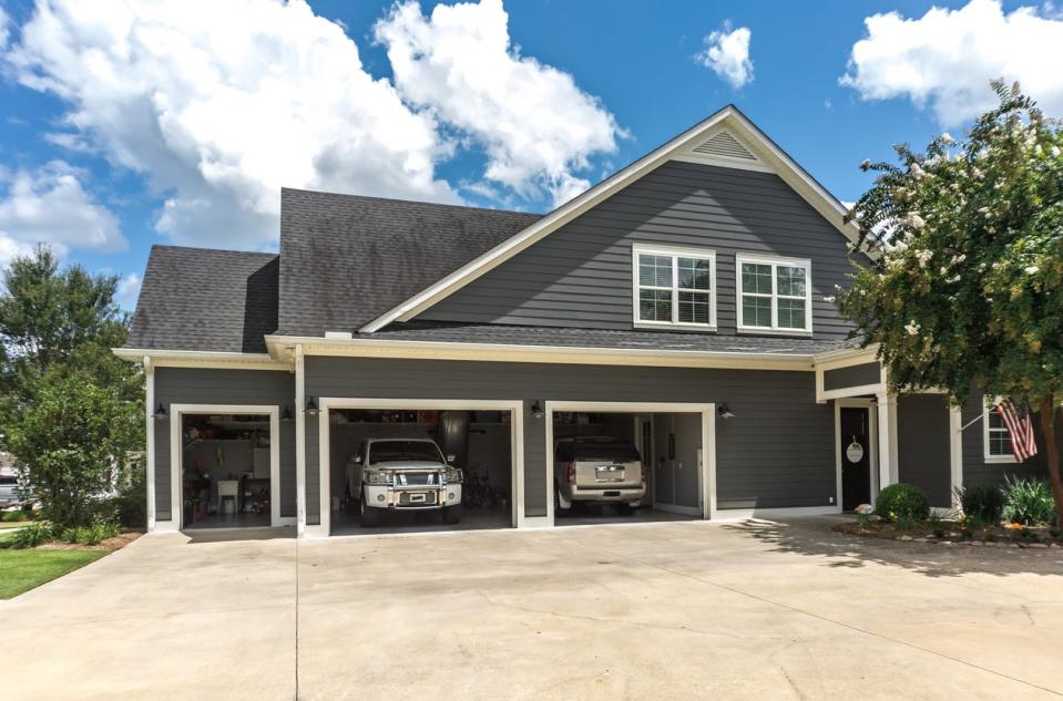 large grey house with driveway and two cars parked in open garage 