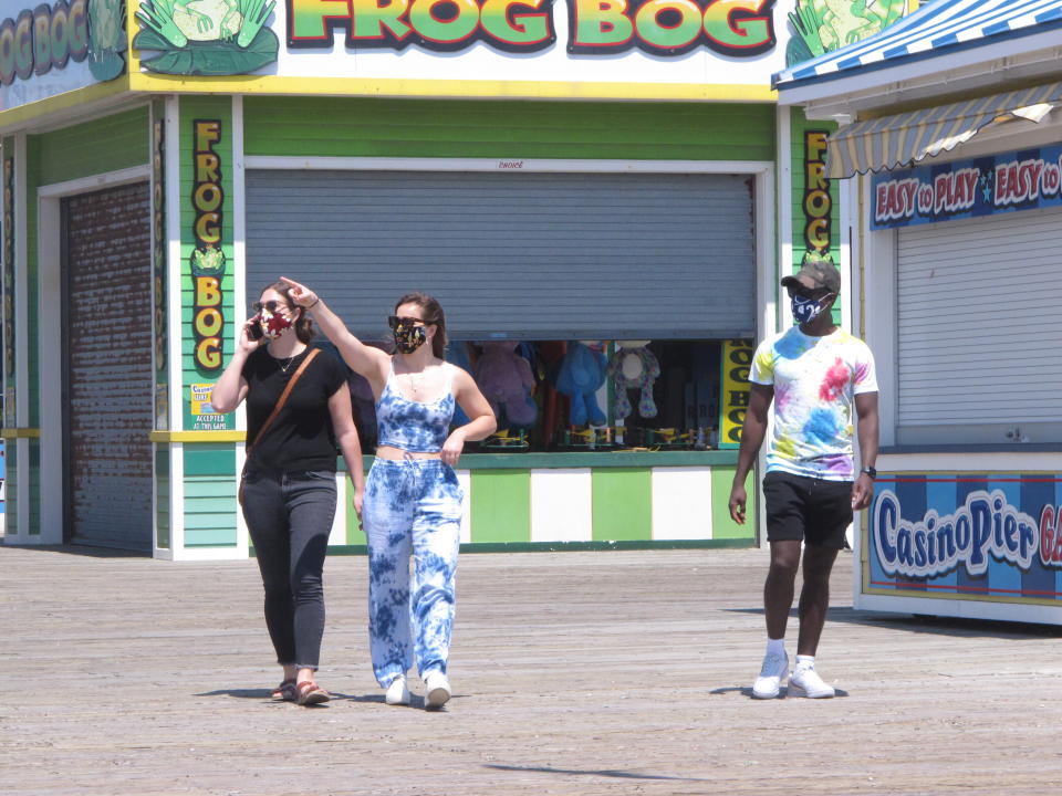 People wearing masks walk on the boardwalk in Seaside Heights, N.J. on Friday, May 15, 2020, the on the first day it opened during the coronavirus outbreak. It and another popular Jersey Shore beach, Point Pleasant Beach, were among those allowing people back onto the sand with some restrictions to try to slow the spread of the virus. (AP Photo/Wayne Parry)