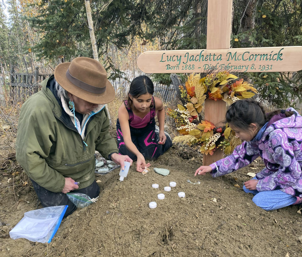 In this Sept. 29, 2023, photo at the grave of Lucky Pitka McCormick, her granddaughter Kathleen Carlo, left, and McCormick's great-great-grandchildren Lucia, center, and Addison Carlo place candles and stones on the grave during a reburial ceremony in Rampart, Alaska. Pitka was one of the Lost Alaskans sent to a mental hospital in the 1930s. Her grave was recently discovered, and family members brought her back to Alaska for a proper burial. (Wally Carlo via AP).