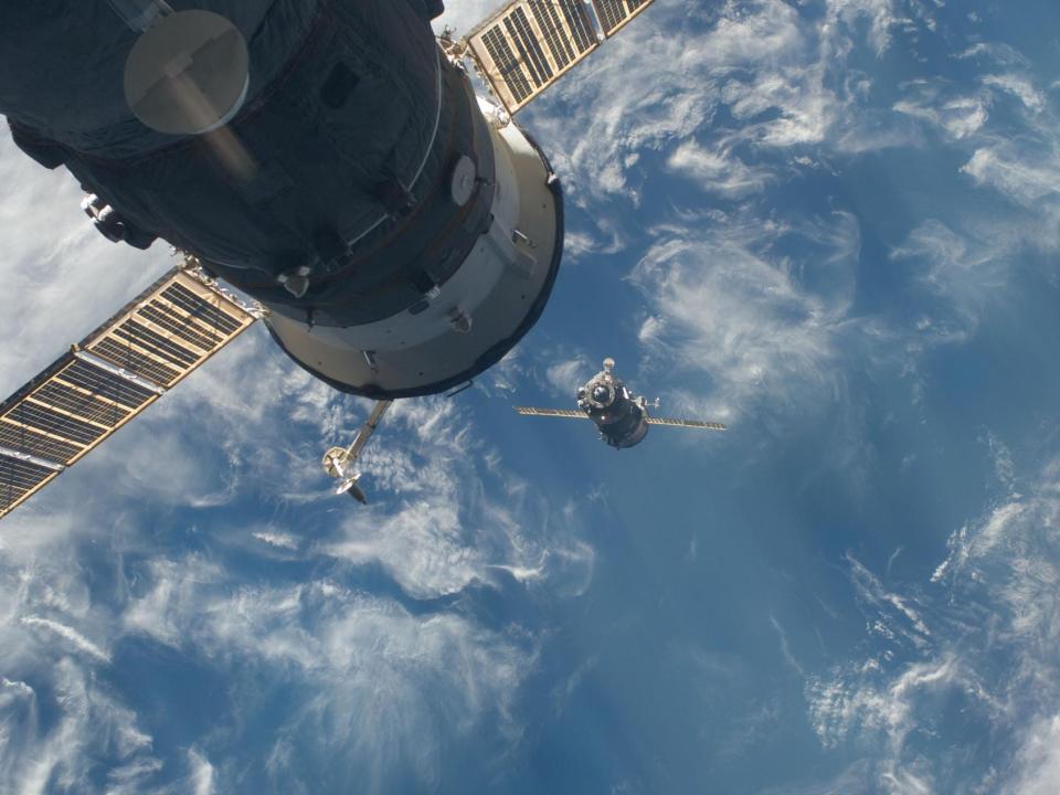 soyuz spacecraft approaches zarya module cylinder with solar panels above blue earth oceans