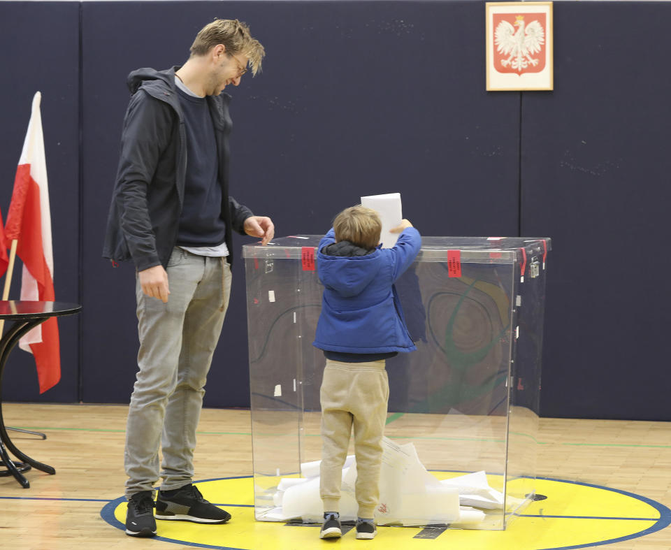 A man lets his son help him cast his ballot in elections to the Polish parliament in Warsaw, Poland, on Oct. 13, 2019. Poles are voting Sunday in a parliamentary election, that the ruling party of Jaroslaw Kaczynski is favored to win easily, buoyed by the popularity of its social conservatism and generous social spending policies. Critics, however, fear that another term for the party, whose term has included an erosion of the rule of law, will mark a further decline in democracy. (AP Photo/Czarek Sokolowski)