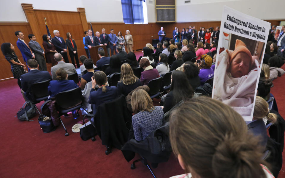 A demonstrator holds a sign as Virginia Gov. Ralph Northam, at podium, gestures during a press conference at the Capitol in Richmond, Va., Thursday, Jan. 31, 2019. Northam made a statement and answered questions about the late term abortion bill that was killed in committee. (AP Photo/Steve Helber)