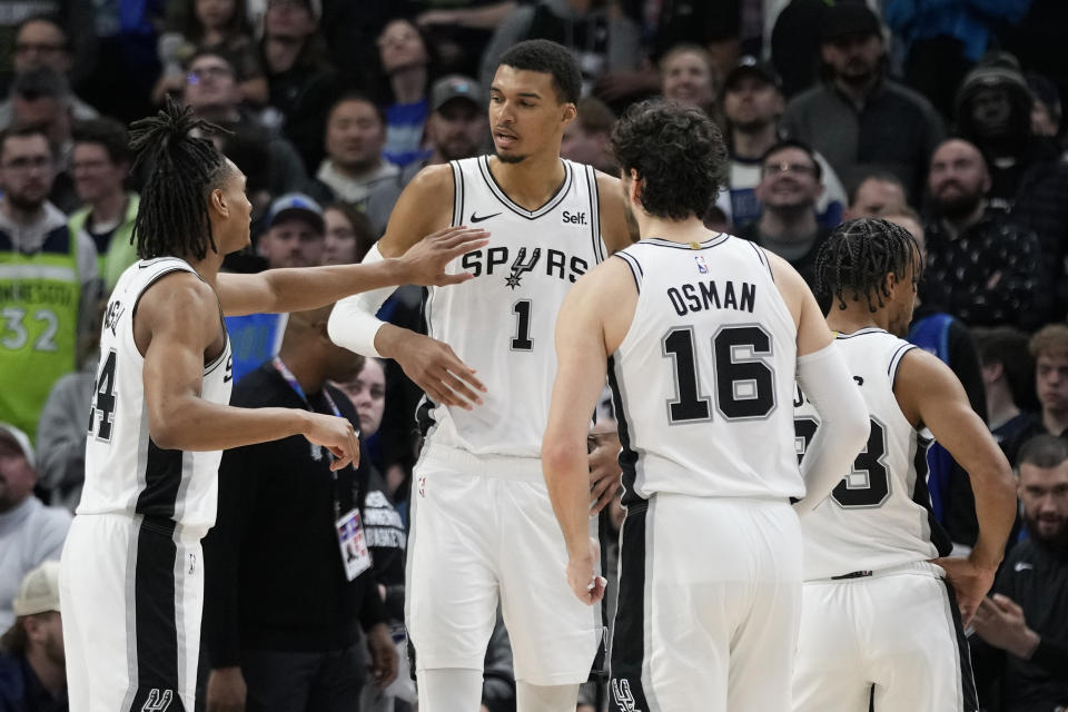 San Antonio Spurs guard Devin Vassell, left, center Victor Wembanyama (1) and forward Cedi Osman (16) talk during the second half of an NBA basketball game against the Minnesota Timberwolves, Wednesday, Dec. 6, 2023, in Minneapolis. (AP Photo/Abbie Parr)