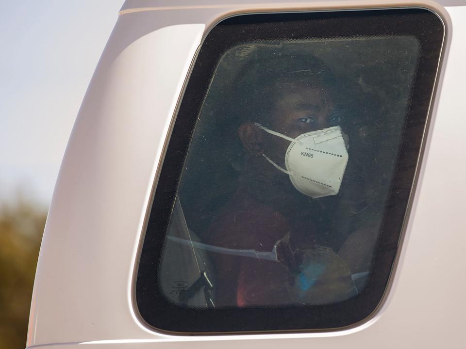 A man wearing a face mask looks out the window of a white van.